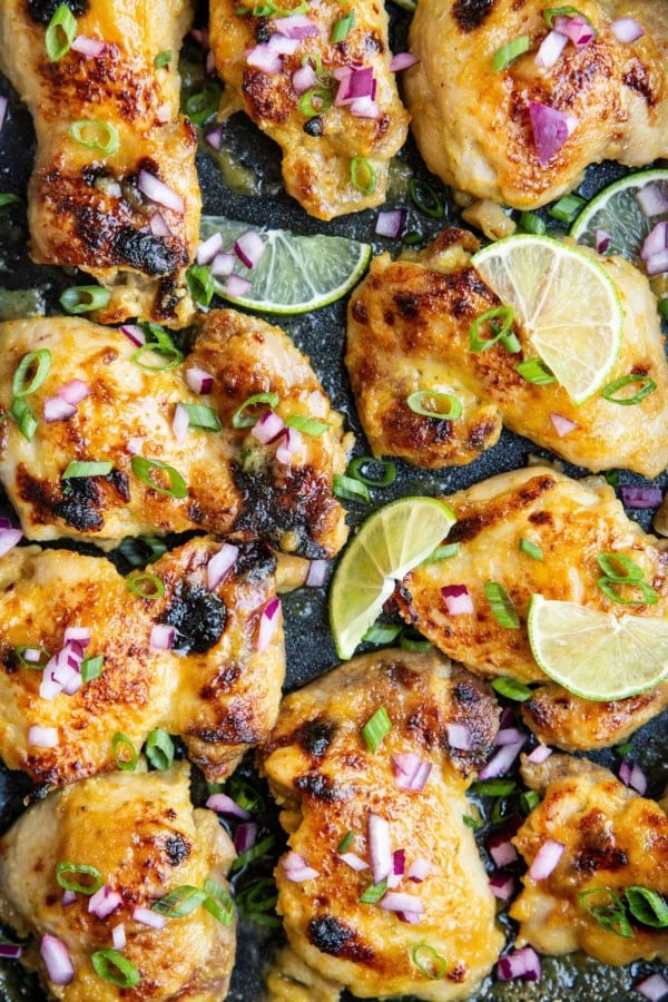 Chicken thighs in a casserole dish, sprinkled with green onions, red onions and lime slices.