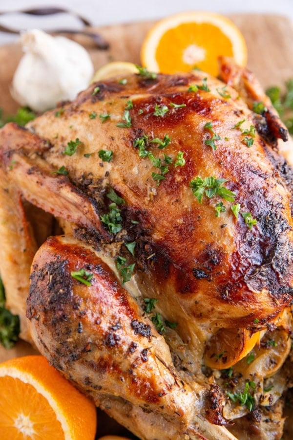 Whole roast turkey on a wooden cutting board with sliced oranges and fresh garlic in the background.