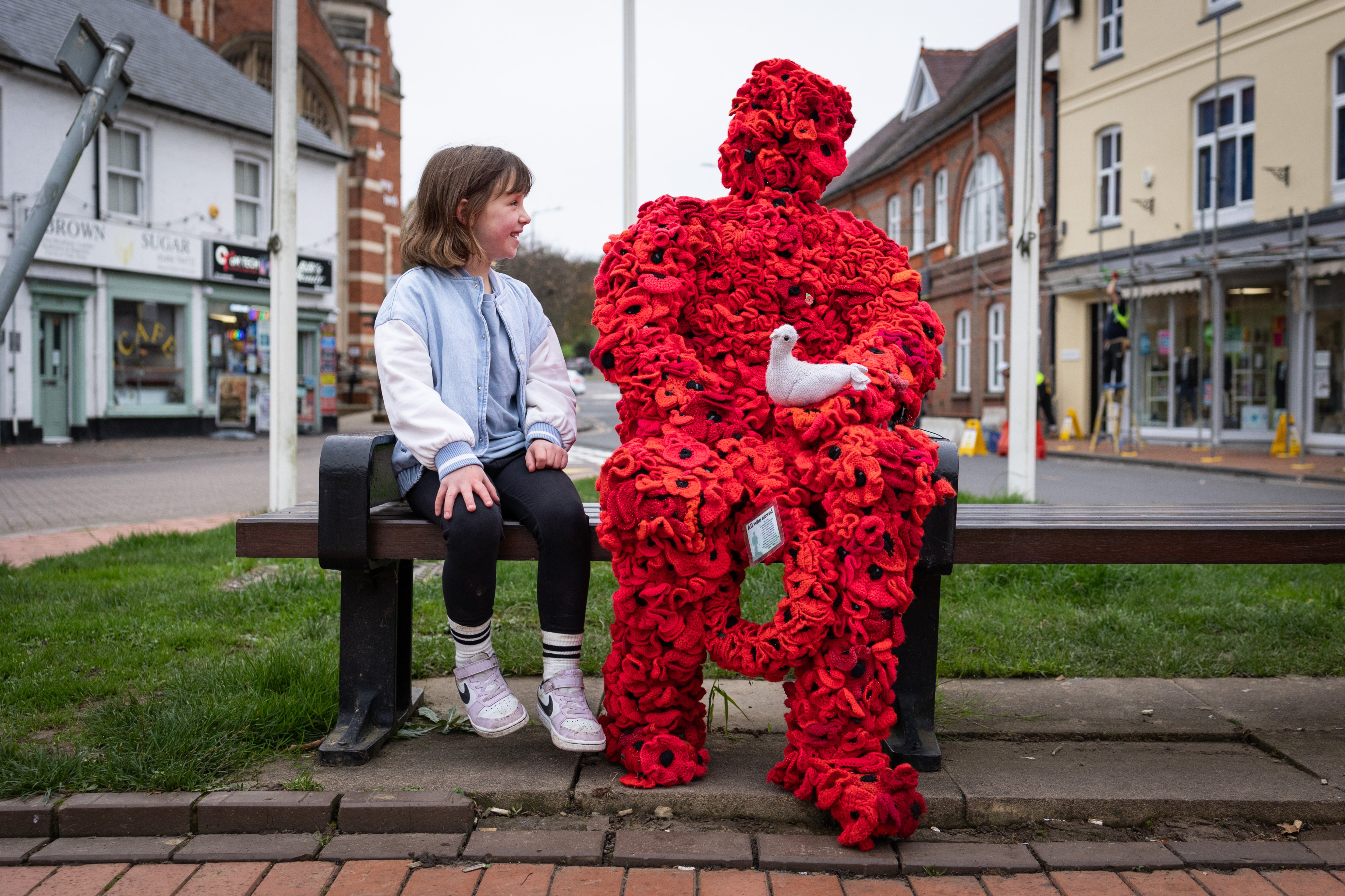 Grace Smith, six, sits next to an installation made of knitted poppies at a war memorial in Chesham, Buckinghamshire. She thought the piece was “really cool”