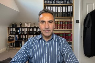 a man in a striped shirt stands in front of a bookshelf with binders labeled with the numbers 25 29 and 29