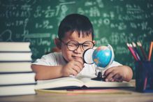 Boy Studying at Table Against Blackboard