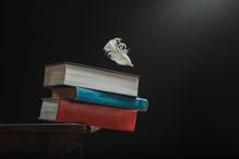 A stack of books balancing on the edge of the table and a feather dropping on them threatening to upset the delicate balance. Conceptual photo