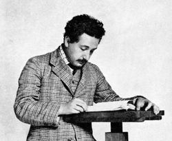 A picture of Albert Einstein, standing, reading a book.