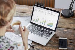 Businesswoman drinking tea and reviewing data at laptop