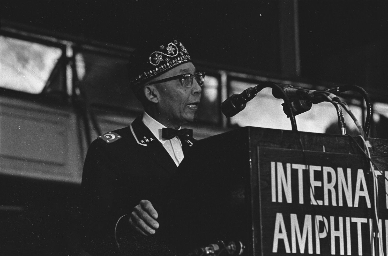 Elijah Muhammad standing at a podium and speaking into a microphone