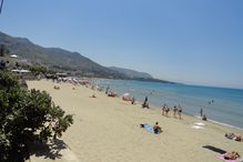 Italian beach with people on the sand and in the water under a cloudless blue sky.