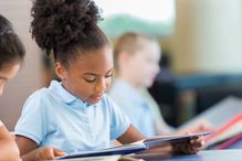 Adorable African American girl reading books in the school library