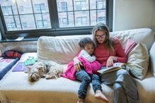 Young girl and her mom reading together on a couch with dog nearby