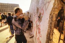 People hitting the Berlin Wall with hammers between Brandenburg Gate and Reichstag.