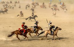 Dozens of Mongolian riders on horses racing across the sand.
