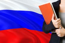 Learning Russian language concept. Young woman standing with the Russia flag in the background. Teacher holding books, orange blank book cover.