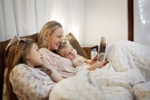 mother reading nursery rhyme on tablet to kids in bed