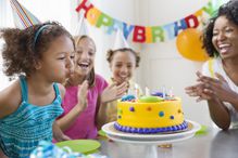 Little girl blowing out birthday candles at party with family and friends