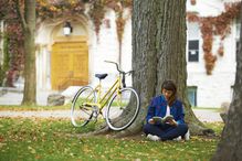 Girl reading book on university campus in fall with yellow bicycle