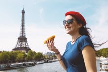 France, Paris, woman with croissant standing in front of Seine river and Eiffel Tower