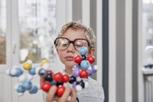 Boy wearing over sized glasses looking at molecular model.