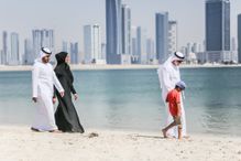 People walking on a beach in Kuwait with the city skyline behind them.