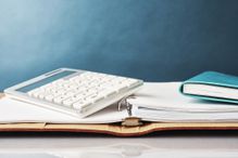 A calculator and notebook are sitting on top of an open binder.