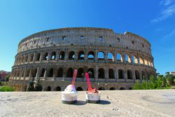 Two cups of ice cream sitting on a ledge in front of the Colosseum in Rome on a sunny day.