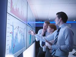 Three Business People Discuss Graphs on Screen in Meeting Room