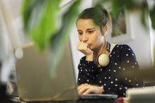 Girl with headphones on neck looking at laptop.