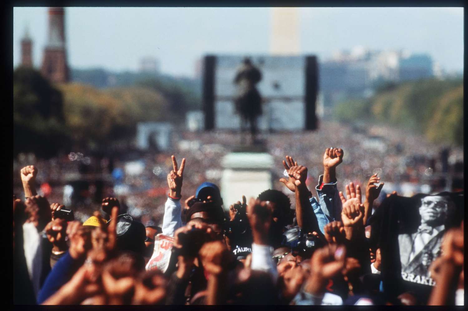 A crowd of thousands of Black people march attendees raise fists and peace signs