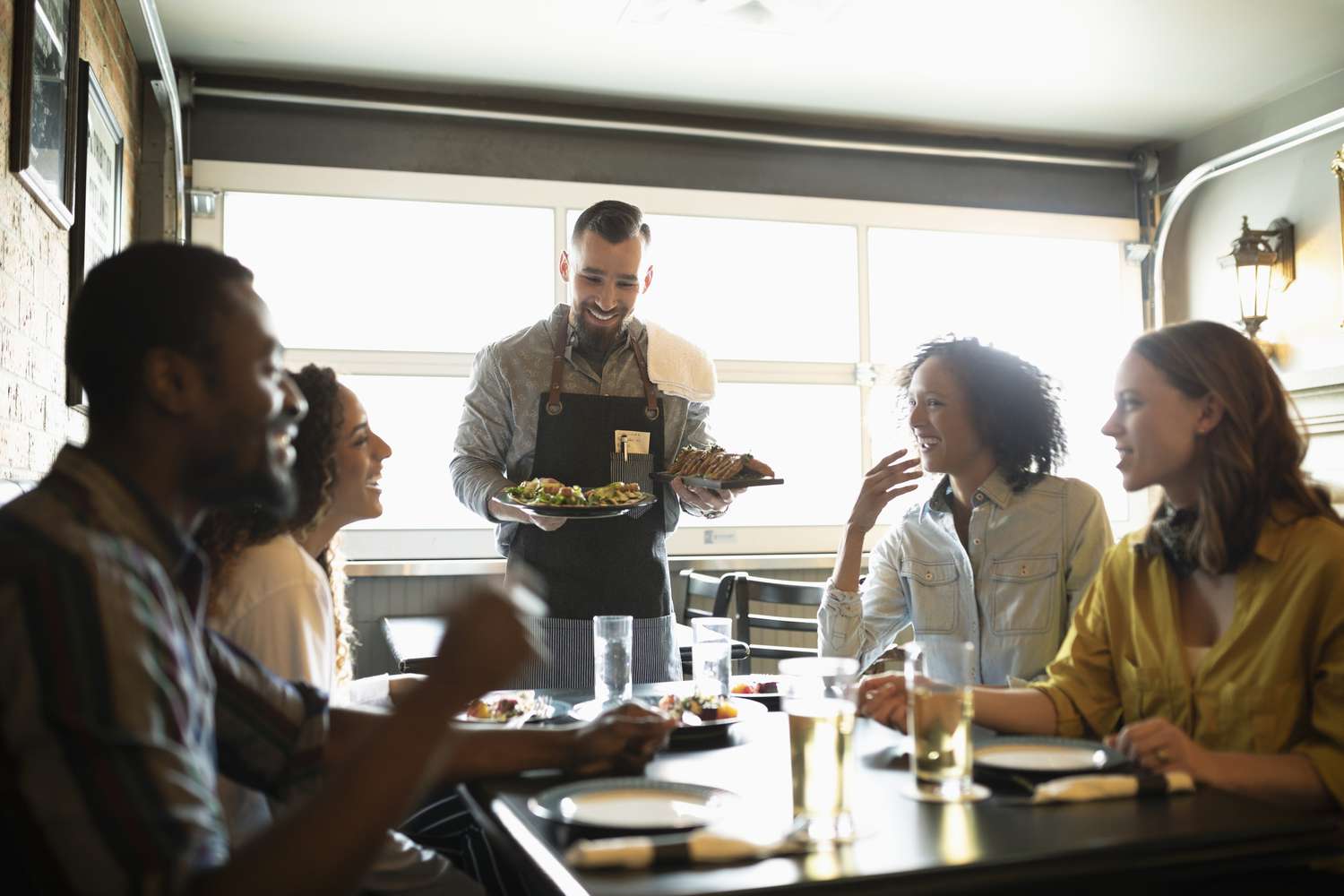 Waiter serving food to friends in restaurant