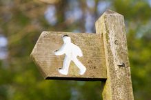 Wooden footpath directional sign showing carving of walking person