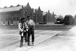 Two servicemen stand beside the Pullman Building and train cars with locked arms and a bottle of liquor during the 1894 Chicago Pullman Strike