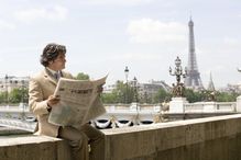 Man reading a French newspaper in Paris with the Eiffel Tower in the background.