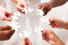 Hands of different skin color holding puzzle pieces of the same puzzle