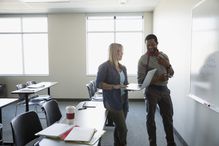 Professor and adult education student with laptop at whiteboard in classroom