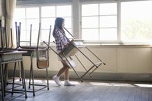 Girl (6-8) carrying desk and chair in classroom