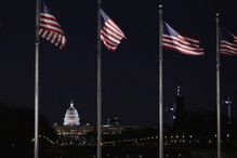 Four American flags flying with the Capitol building in the background