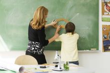 Teacher helping boy draw angle on blackboard using protractor, rear view