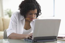 A woman with a pencil in her mouth is hard at work on her computer