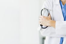 Doctor holding a stethoscope standing before a white background.