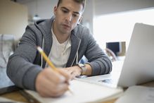 Person writing in notebook at laptop