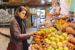 A woman chooses from different produce options at a market.