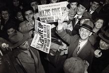 New Yorkers celebrate V-E Day and the end of WWII, holding up newspapers and smiling, black and white photograph.