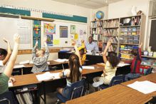 Schoolchildren raising hands for teacher in classroom