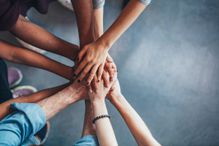 A close-up of a group of people who are standing in a semi-circle and have placed their outstretched hands on top of each other.