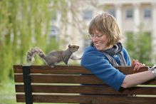 Woman and squirrel on a park bench in an urban area