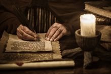 Man writing on parchment with a quill pen by candlelight, sepia photograph.