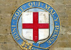 English symbol bearing the words "Honi Soit Qui Mal Y Pense" on a brick wall.