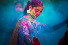 Vivid color photograph of an Indian woman dancing, covered in paint against a blue background.