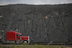 Semi truck passing in front of a mound of newly-mined coal