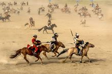 Dozens of Mongolian riders on horses racing across the sand.