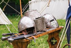 Close-Up Of Medieval Helmets And Swords On Table.