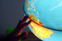 A child's hand runs along the equatorial seam of an illuminated globe